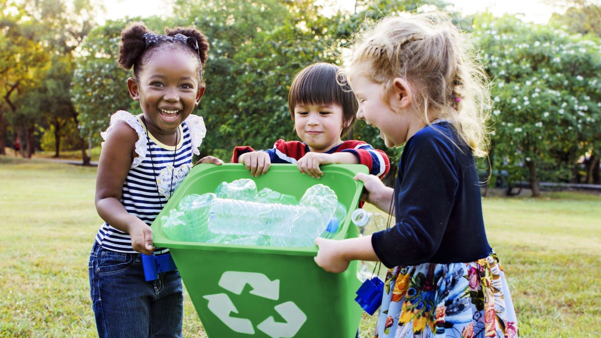 Children around recycling bin showing children working together to help the environment.